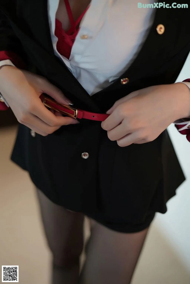 A woman in a black skirt and a white shirt is holding a red belt.