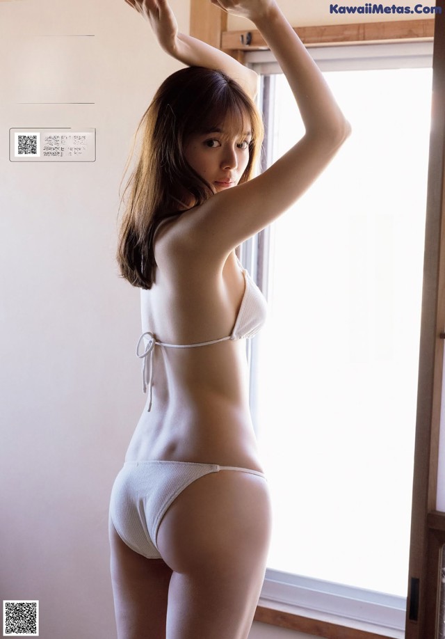 A woman in a white bikini standing by a window.