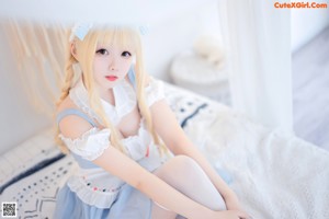 A woman in a blue dress sitting on a bed holding a white rabbit.