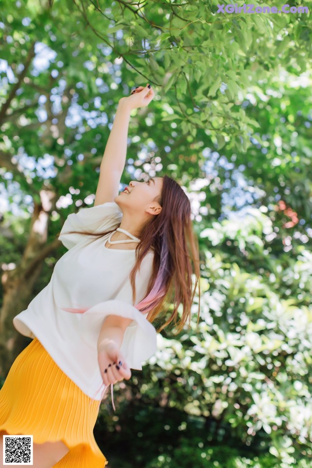 A woman in a white shirt and yellow skirt standing under a tree.