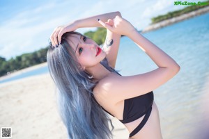 A woman with blue hair posing on a beach.
