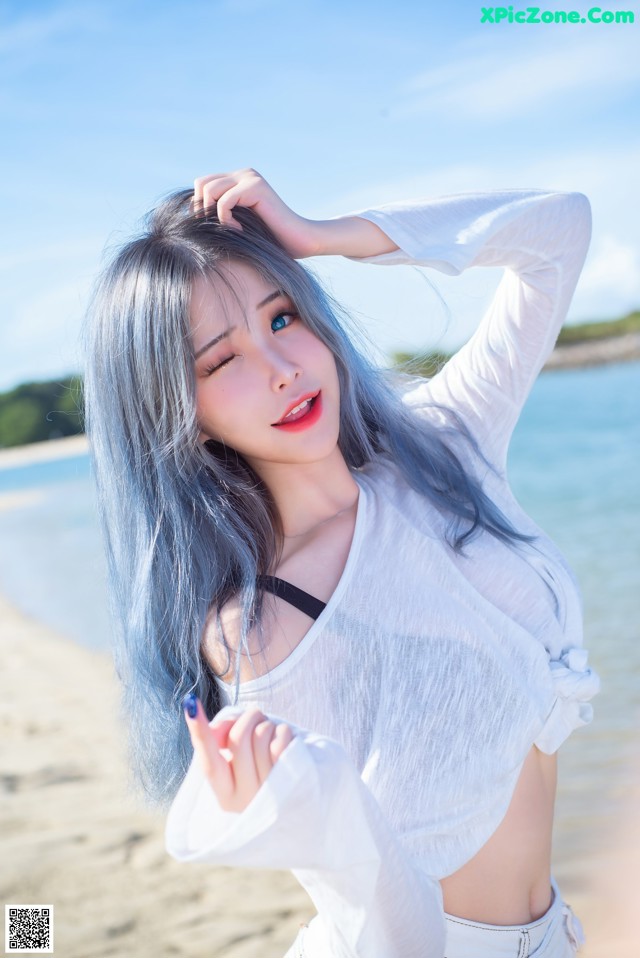 A woman with long blue hair standing on a beach.