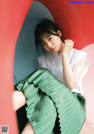 A young woman sitting on a bed with her hand on her chin.