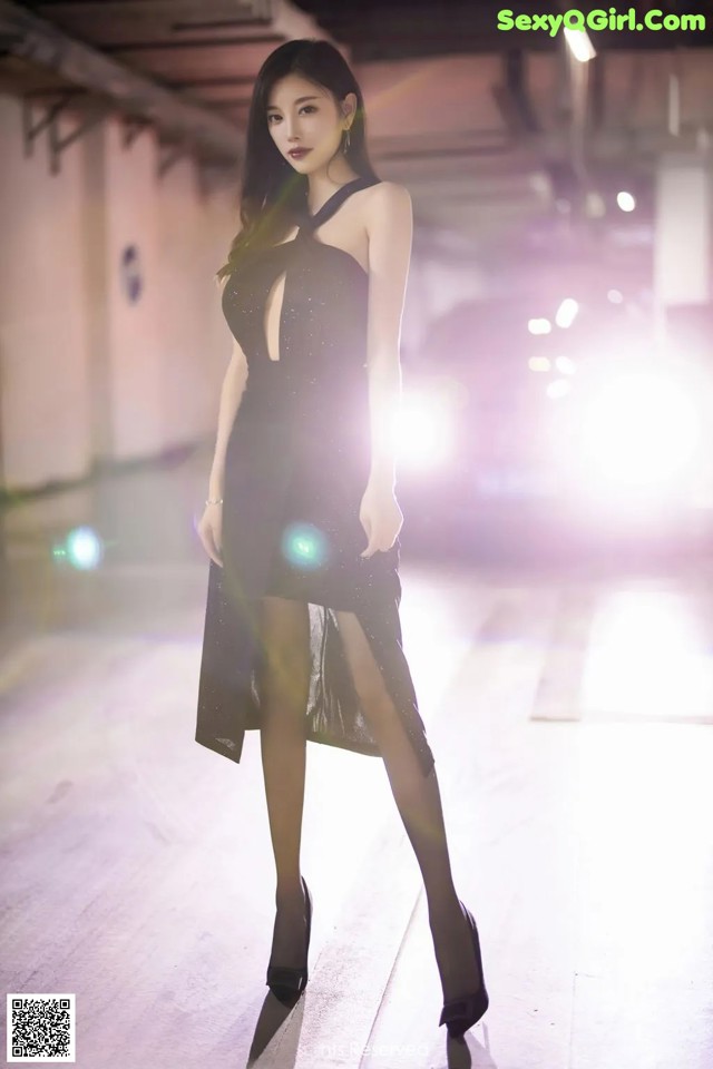 A woman in a black dress standing in a parking garage.