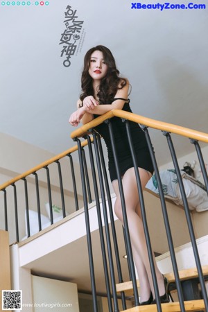 A woman in a black dress sitting on a white couch.