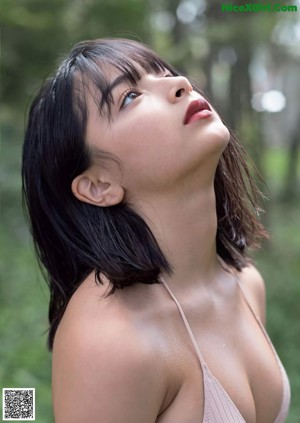 A woman in a bikini standing in the woods.