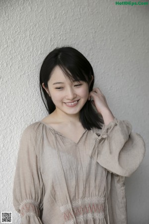 A woman with long black hair standing in front of a wall.