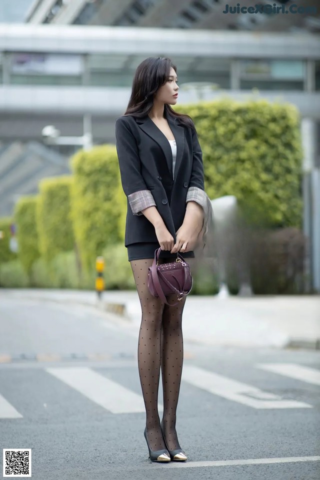 A woman in a black blazer and polka dot tights is standing on the street.