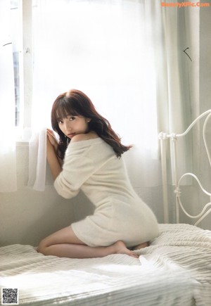 A woman laying on top of a bed in a white sweater.