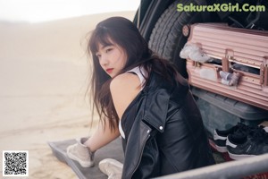 A woman in a black leather jacket sitting on a bench.