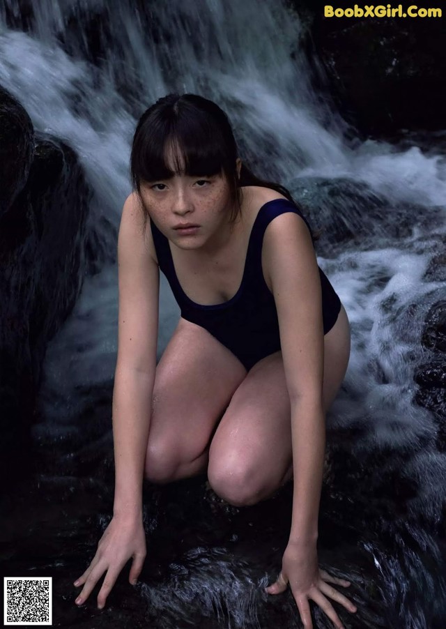 A woman in a black bathing suit crouching down in a stream.