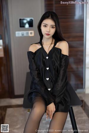 A woman in a pink dress sitting on a bed.